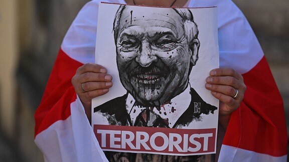 Person hält Poster mit blutigem Bild von Lukaschenko und dem Schriftzug 'Terrorist'