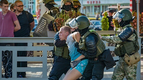 Polizeieinsatzkräfte in Minsk kämpfen mit einem Mann auf der Straße.