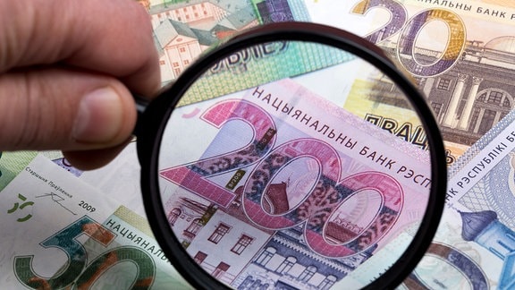 Eine Person hält eine Lupe über belarussische Rubelscheine.