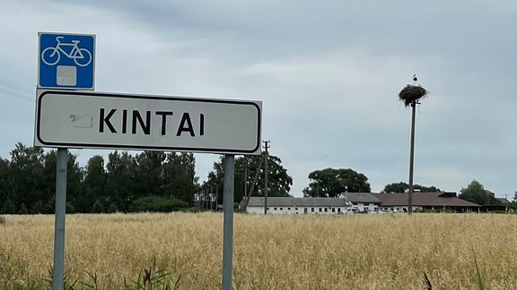 Auf einem weißen Ortsschild in einer trostlos erscheinenden Landschaft steht Kintai, darüber ein Schild mit einem Fahrrad