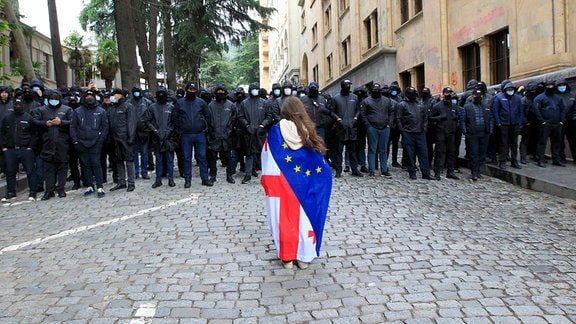 Ein Demonstrant mit drapierten georgischen National- und EU-Flaggen steht vor der Polizei