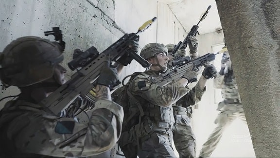 NATO-Soldaten im Kampfanzug mit Maschinenpistolen im Anschlag gehen eine Treppe hinauf