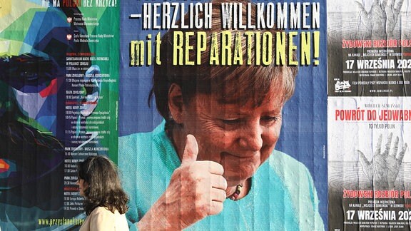 Plakat zeigt Foto von Angela Merkel und Text "Angela Merkel - Herzlich Willkommen mit Reparationen!"