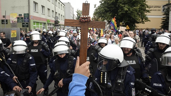 Ein Arm hält ein Holzkreuz, um welches ein Rosenkranz gewickelt ist, bei einem LGBT-Marsch für Gleichberechtigung.