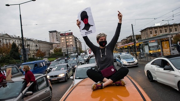 Demonstrantin sitzt auf Autodach und hält ein Plakat.