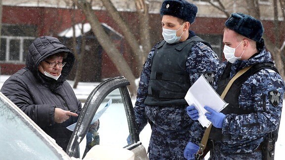 Zwei Polizisten mit Mundschutz kontrollieren in Moskau eine Autofahrerin
