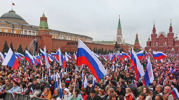 Menschen schwenken Fahnen, während sie sich zu einem Konzert versammeln, um den Beitritt neuer Gebiete zu Russland auf dem Roten Platz in Moskau zu feiern.