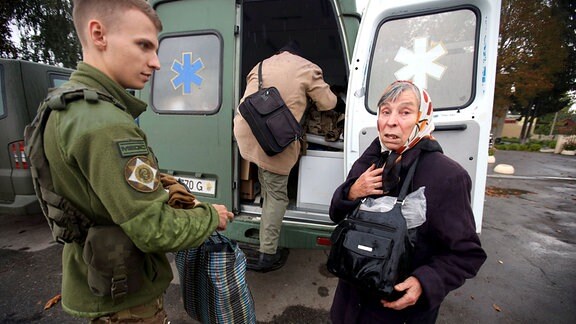 Eine Frau steht nach der Befreiung von Kozacha Lopan, Region Charkiw, von einem Krankenwagen. Neben ihr ein Soldat.