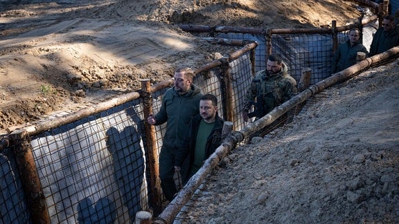 Der ukrainische Präsident Wolodymyr Selenskyj und zwei weitere Männer gehen durch einen Schützengraben in der Region Tschernihiw.