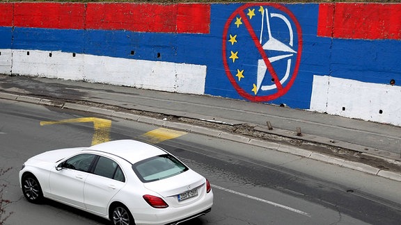 Ein Auto fährt an einem antieuropäischen und Anti-NATO-Wandgemälde vorbei.