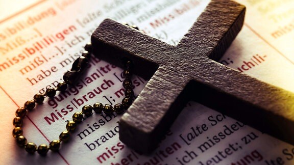  Symbolfoto Missbrauchsskandal - Kreuz auf einem Wörterbuch mit dem Wort Missbrauch