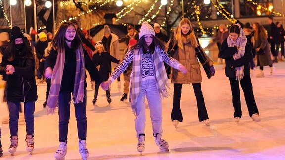 Mädchen laufen Schlittschuh auf weihnachtlich dekorierter Eisfläche