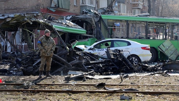 Ein Soldat steht inmitten von zerstörten Gebäuden und Fahrzeugen