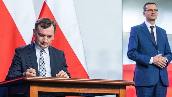 Polens Justizminister Zbigniew Ziobrio unterzeichnet den Koalitionsvertrag. Im Hintergrund Ministerpräsident Mateusz Morawiecki.