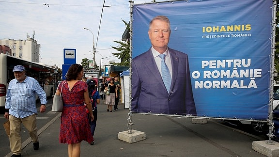 Straßenszene - Fußgänger laufen an einem Wahlplakat in Bukarest vorbei, das Klaus Iohannis zeigt