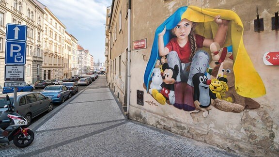 Graffiti an einem Haus, dass ein Mädchen mit Kuscheltieren und einer Ukrainischen Flagge zeigt
