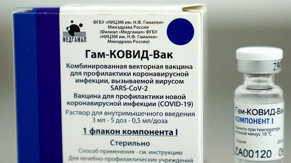 Eine Ampulle des russischen Impfstoffes Sputnik V, daneben eine Verpackungsschachtel mit russischer Schrift.
