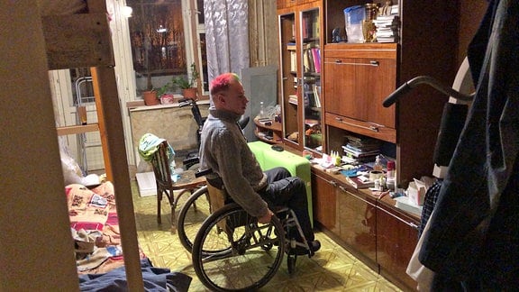 Ein Rollstuhlfahrer sitzt vor einer Schrankwand. Links ist der Ansatz eines Hochbettes zu erkennen.