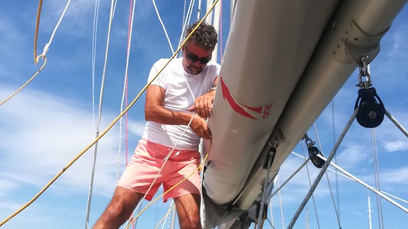 Mann mit rosa Shorts und weißem Shirt auf Segelboot