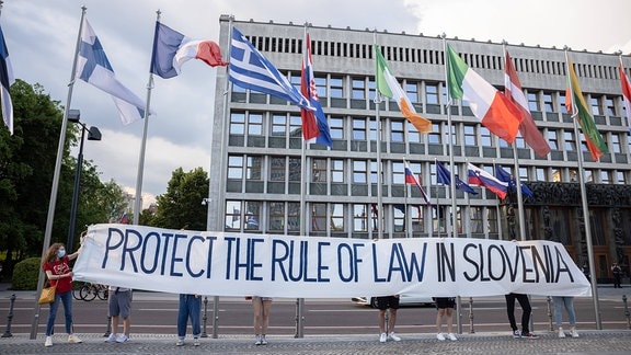 Demonstranten halten ein Banner mit der Aufschrift 'Schützt die Rechtsaatlichkeit in Slowenien'.
