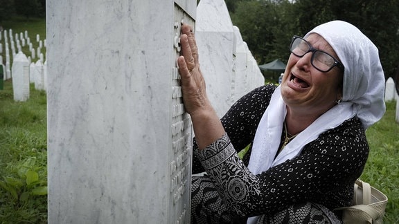 Frau weint an einem Grabstein
