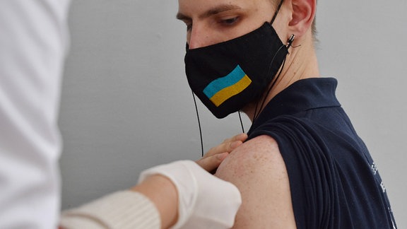 Ein junger Mann mit Maske bekommt eine Impfung