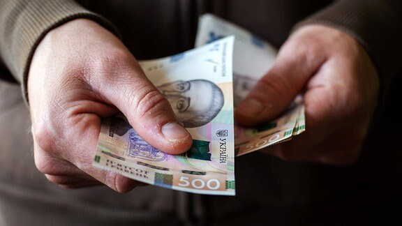 Ein Mann hält Ukrainische Geldscheine in den Händen.