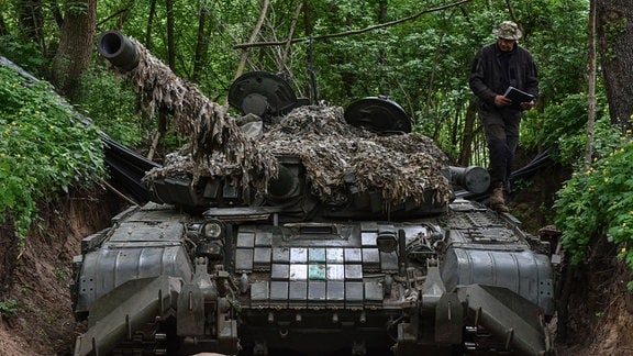 Ein ukrainischer Soldat steht in einem Wald neben seinem Panzer.