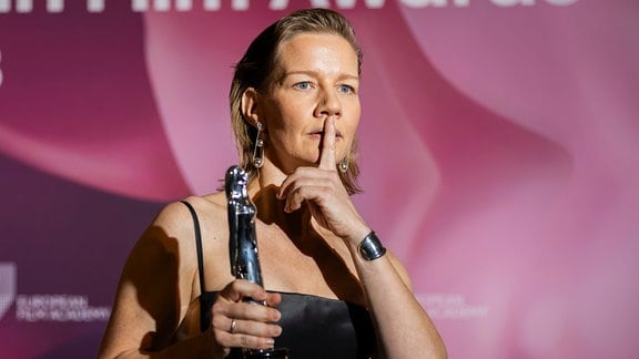 Sandra Hüller, eine Frau hält eine Trophäe in der Hand und hält einen Finger vor den Mund.