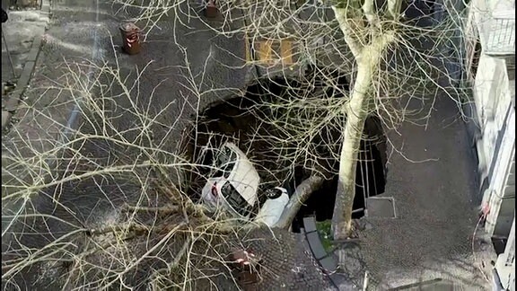 Ein mehrere Meter tiefes, großes Loch, das sich auf einer Straße und zum Teil auf dem Bürgersteig aufgetan hat - darin zwei umgestürzte Autos