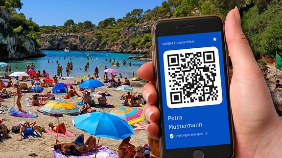 Symbolbild: Ein digitaler Impfpass auf dem Smartphone vor einem Strand mit vielen Besuchern.  