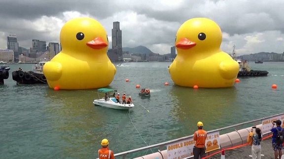 Zwei riesige Gummi-Enten schwimmer in einem Hafenbecken.