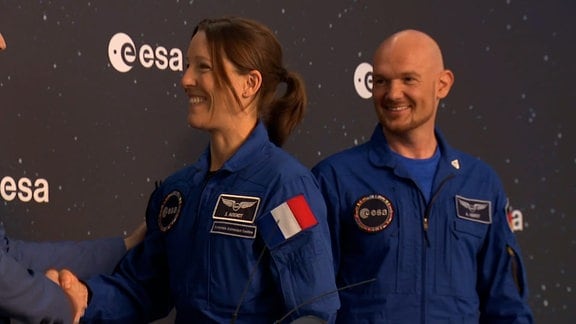 Astronautin nimmt Zeugnis entgegen. Ausbilder Alexander Gerst im Hintergrund.
