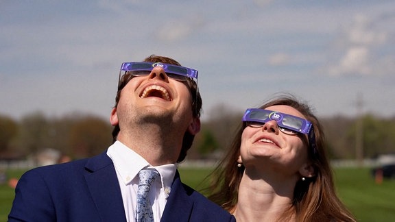 Ein Mann und eine Frau, die eine besondere Brille aus Pappe tragen, schauen strahlend Richtung Himmel