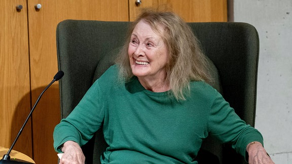 Eine ältere Frau sitzt in einem Stuhl und lächelt