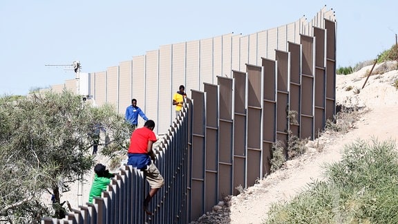 Migranten klettern über einen Zaun auf der Insel Lampedusa