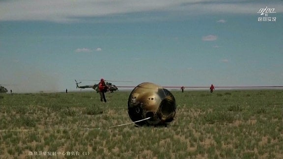 Eine verbrannte Kapsel liegt in der mongolischen Steppe. Im Hitnergrund ein Transporthubschrauber. 