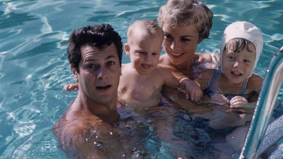 Ein Mann und eine Frau mit zwei Kindern im Swimming-Pool schauen in die Kamera