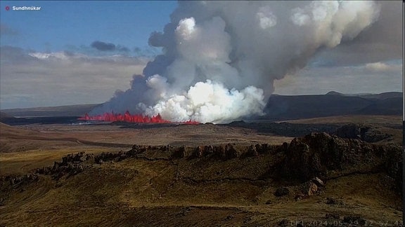 Vulkan spuckt rote Lava. Darüber riesige weiße Wolke.