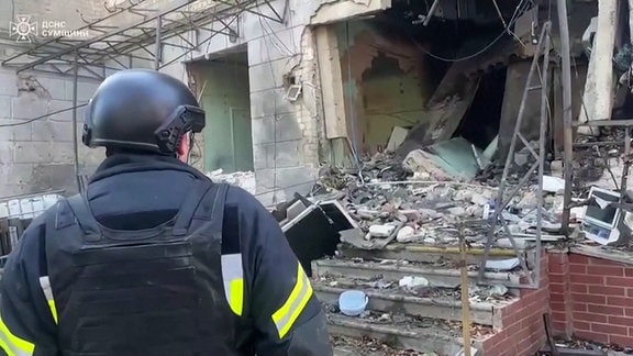 Ein ukrainischer Feuerwehrmann vor einem in Teilen zerstörten Haus.