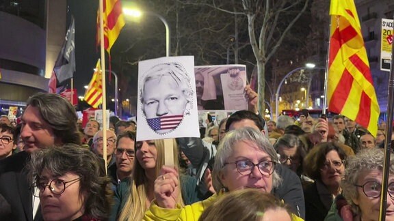 Viele Menschen protestieren auf der Straße.Sie halten Plakate hoch mit Bildern von Julian Assange.