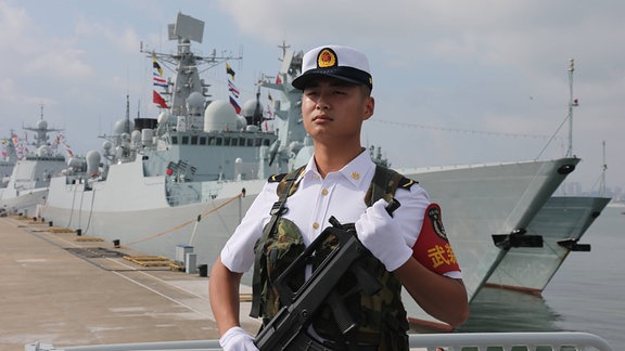 Ein chinesischer Soldat steht vor einem Kriegsschiff