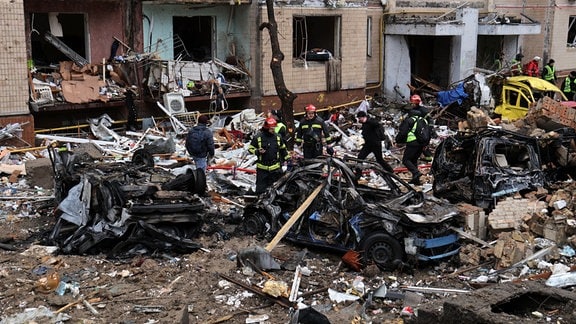 Rettungskräfte stehen inmitten von Trümmern neben einem beschädigten Wohngebäude nach einem russischen Raketenangriff. 