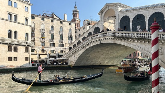 Eine Gondel mit Touristen vor der Rialto-Brücke im Zentrum von Venedig.