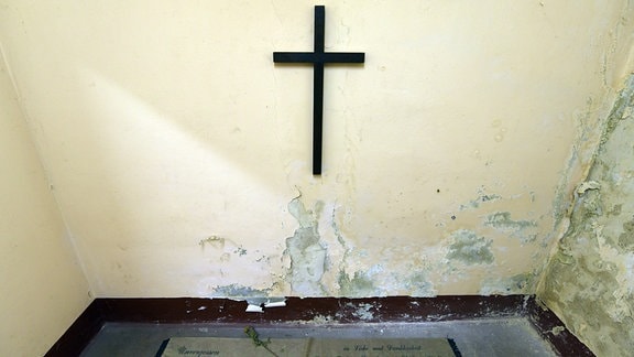 Ein Raum mit einem Kreuz an der Wand und ein Trauerband mit der Aufschrift Unvergessen