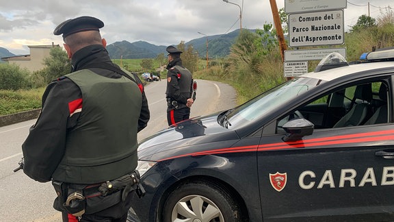 Italienische Polizisten stehen neben einem Polizeiauto am Ortseingang von San Luca.