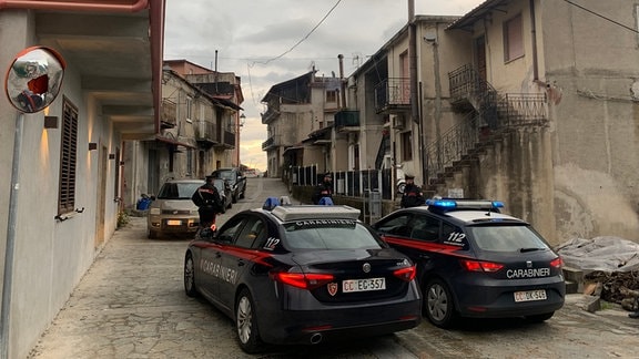 Autos der italienischen Polizei stehen in einer Straße mit mehreren Häusern in San Luca.