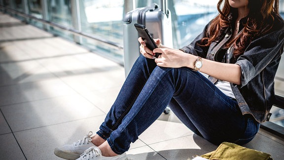 Junge Frau mit Tasche und Koffer, die in der Flughafenlounge auf den Abflug wartet.