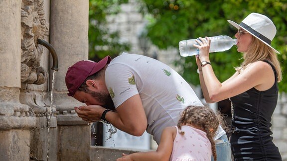 Ein Mann kühlt sich ab, während eine Frau kaltes Wasser am Brunnen trinkt