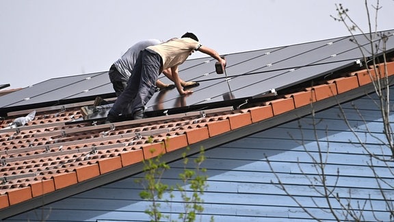 Arbeiter bei der Montage von Solarpanels auf einem Hausdach.